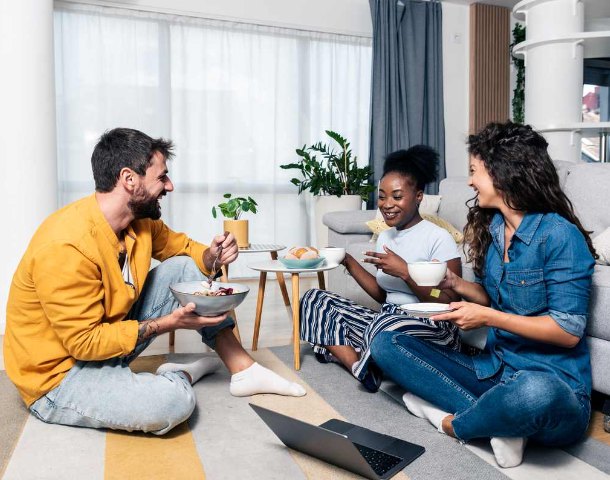 Three friends sharing a meal on the floor of their rented living room